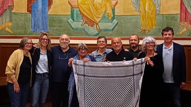 Un gruppo di persone posa con una kefiah davanti ai disegni dei bambini di Gaza